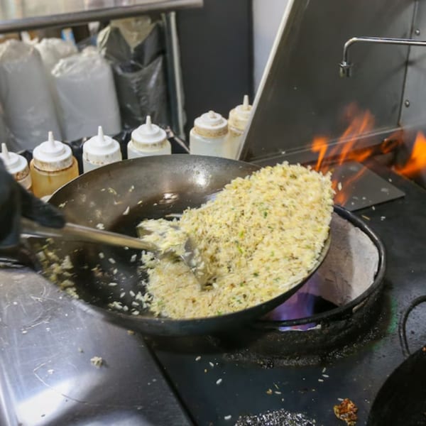 A chef stir-frying fried rice in a large wok over a flaming stove at Bobby Wong's.