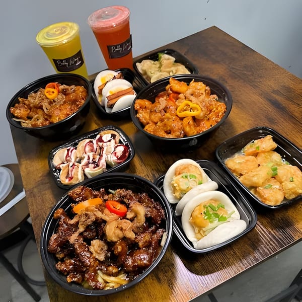 A wooden table laden with various Bobby Wong's Chinese dishes and two colorful drinks.
