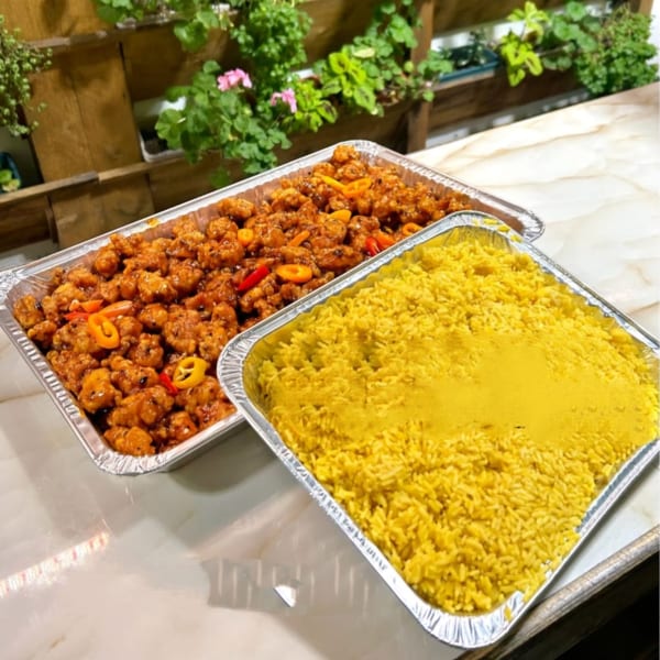Two foil trays of Bobby Wong's Chinese food, one with orange chicken and the other with yellow rice.