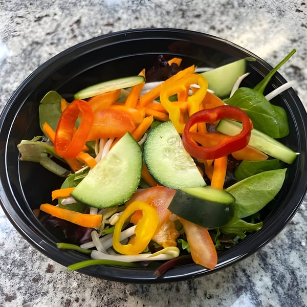 A vibrant Bobby Wong's salad with mixed greens, bell peppers, cucumbers, and tomatoes in a black bowl.