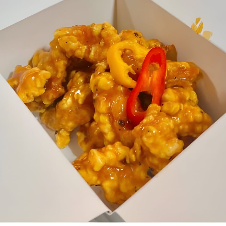 Bobby Wong's sweet and sour chicken in a white takeout box, garnished with red and yellow bell peppers.